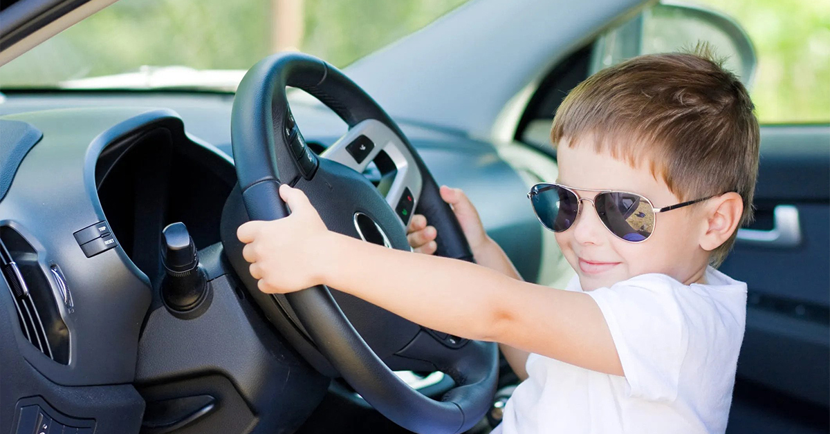 child sitting in front seat of a car holding steering wheel
