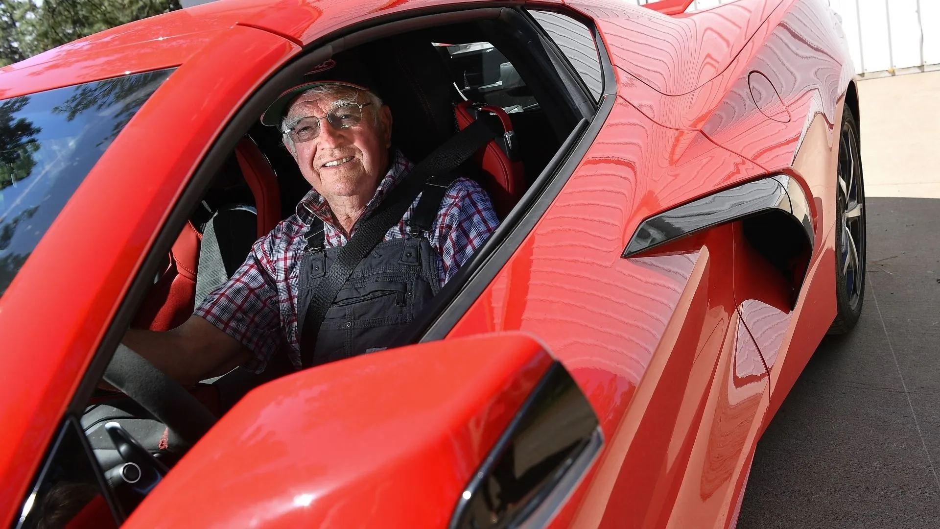 87 year old man in the driver's seat of a red C8 Corvette