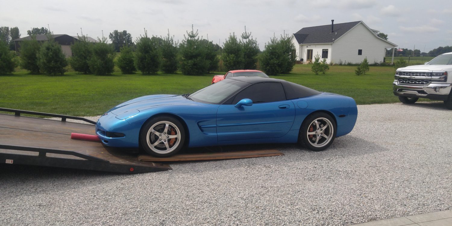 A blue C5 Corvette is being loaded into a tow truck