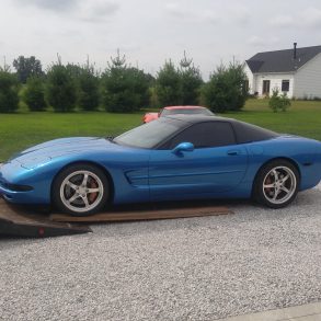 A blue C5 Corvette is being loaded into a tow truck