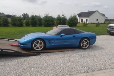 A blue C5 Corvette is being loaded into a tow truck