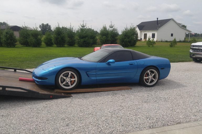 A blue C5 Corvette is being loaded into a tow truck